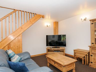 A living room with a blue sofa wooden coffee table tv stand and nested tables at The Shippon in Bude