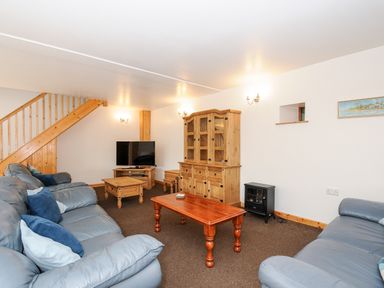 A living room with blue sofas wooden tables a TV a wooden cabinet and stairs at The Shippon in Bude