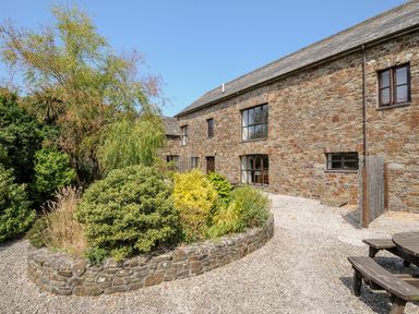 A stone building with multiple windows and a garden area with shrubs and trees at The Shippon in Bude