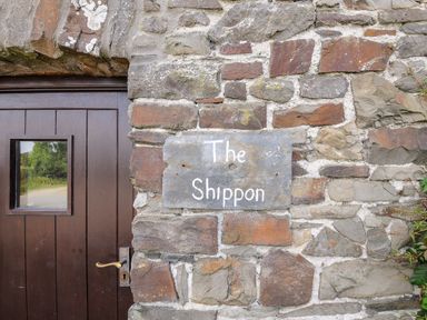 A stone wall with a sign that says The Shippon next to a brown wooden door at The Shippon in Bude