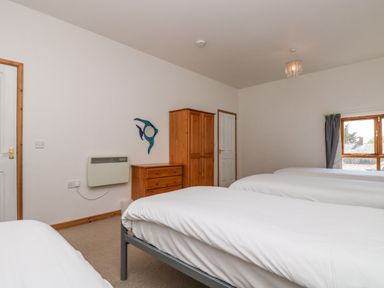 A bedroom with three single beds a wooden wardrobe a wooden chest of drawers and a wall heater at The Shippon in Bude