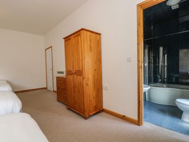 A bedroom with two beds a wooden wardrobe a chest of drawers and an adjacent bathroom with a bathtub and toilet at The Shippon in Bude