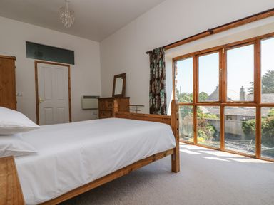 A bedroom with a wooden bed and a large window showing outside greenery at The Shippon in Bude