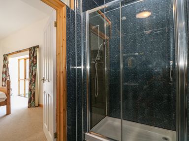 A bedroom with floral curtains and wooden bed frame next to a shower with glass doors at The Shippon in Bude