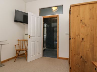 A room with a wooden chair a wall-mounted television an open door leading to a shower area and a wooden wardrobe at The Shippon in Bude