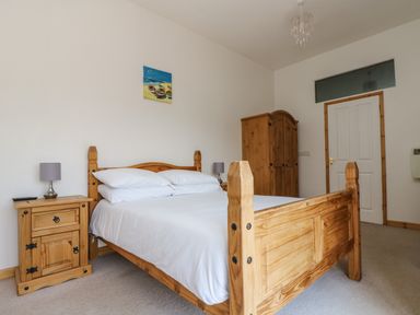 A bedroom with a wooden bed white bedding bedside tables lamps a wardrobe and a door at The Shippon in Bude