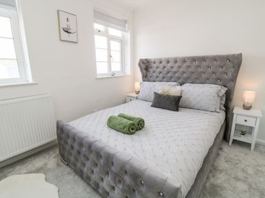 A bedroom with a grey tufted bed and two green towels at Martingale in Torquay
