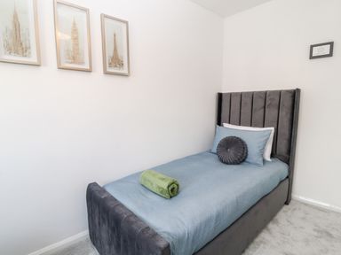 A single bed with blue bedding and a green towel in a small bedroom with white walls and framed pictures at Martingale in Torquay