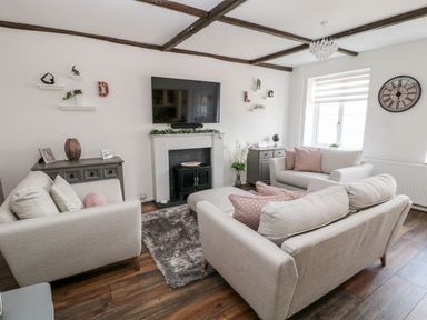 A living room with beige sofas a wall mounted tv a fireplace two sideboards and a window at Martingale in Torquay