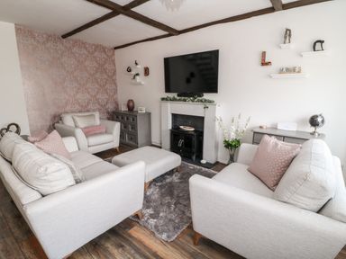 A living room with two armchairs a sofa an ottoman a fireplace a wall-mounted television and wooden flooring at Martingale in Torquay