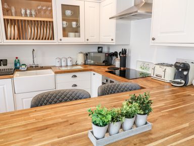 A kitchen with white cabinets wooden countertops a sink microwave kettle toaster coffee machine and potted plants on the island at Martingale in Torquay