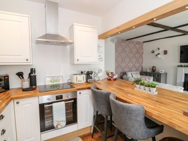 A kitchen with wooden countertops and two gray bar stools opening to a living room at Martingale in Torquay