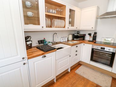 A kitchen with white cabinets wooden countertops a white sink an oven and various kitchenware at Martingale in Torquay