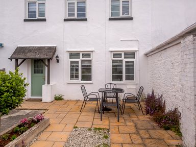 A patio area with a round table and four chairs outside a white building with a green door and three windows at Martingale in Torquay