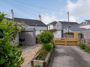 A backyard with a wooden shed a barbecue grill planter box plants and a wooden gate at Martingale in Torquay