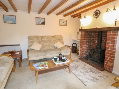 A living room with beige sofas wooden coffee table magazines fireplace and ceiling beams at Primrose Cottage in Stiffkey