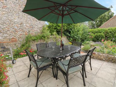 An outdoor patio with a metal table and six chairs under a green umbrella at Primrose Cottage in Stiffkey