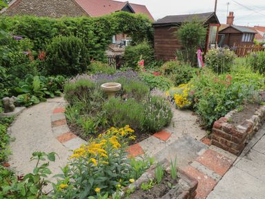 A garden with pathways flowers bushes and a birdbath at Primrose Cottage in Stiffkey
