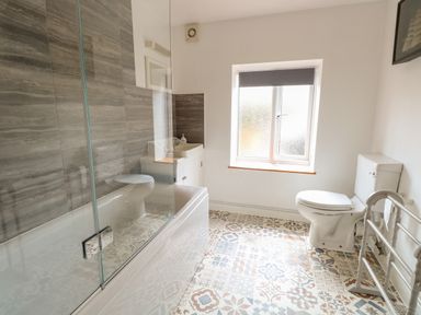 A bathroom with a bathtub shower combination sink toilet window and patterned tiled floor at Primrose Cottage in Stiffkey