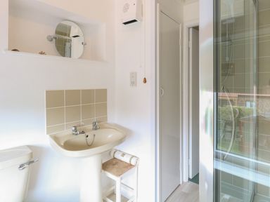 A bathroom with a sink a toilet a small stool and a glass shower door at Primrose Cottage in Stiffkey