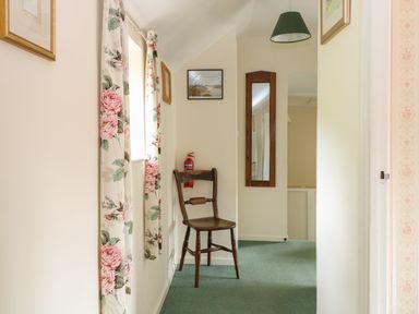 A hallway with floral curtains a wooden chair a wall mirror and a ceiling light at Primrose Cottage in Stiffkey
