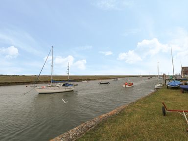 A river with boats moored along the bank and grassy shore at Primrose Cottage in Stiffkey
