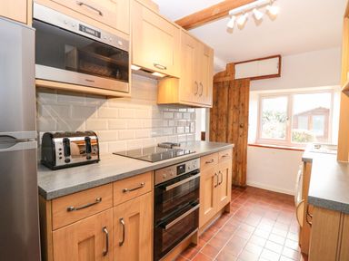 A kitchen with wooden cabinets stainless steel appliances and a window at Primrose Cottage in Stiffkey