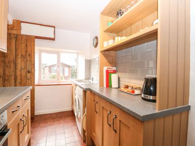 A kitchen with wooden cabinets a washing machine a window and kitchen appliances at Primrose Cottage in Stiffkey