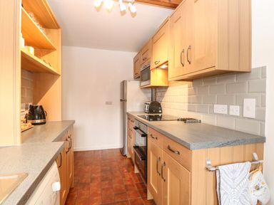 A kitchen with wooden cabinets, gray countertops, an oven, a toaster, a kettle, and a refrigerator at Primrose Cottage in Stiffkey