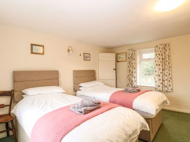 A bedroom with two single beds with pink throws and towels on beds at Primrose Cottage in Stiffkey