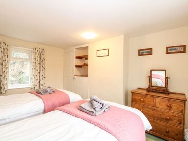 A bedroom with two single beds with pink blankets and towels on top a wooden dresser with a mirror and framed pictures on the wall at Primrose Cottage in Stiffkey