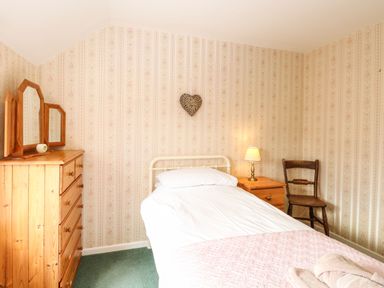 A bedroom with a single bed a wooden chair a wooden dresser with mirror and a bedside table with lamp at Primrose Cottage in Stiffkey