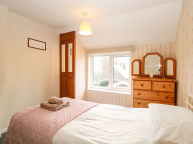 A bedroom with a bed, folded towels, wooden wardrobe, wooden dresser with mirror, and window at Primrose Cottage in Stiffkey