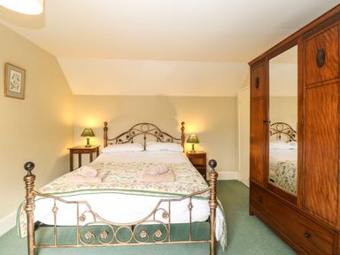 A bedroom with a metal bed frame two bedside tables with lamps and a wooden wardrobe with mirror at Primrose Cottage in Stiffkey