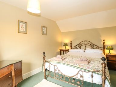 A bedroom with a metal bed frame two bedside tables with lamps and a wooden dresser at Primrose Cottage in Stiffkey