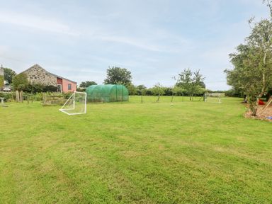 A garden area with two small soccer goals a greenhouse and trees at Llofft Yr Yd in Llandwrog near Dinas Dinlle