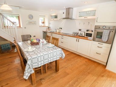 A kitchen with wooden floor white cabinets dining table with tablecloth and staircase at Llofft Yr Yd in Llandwrog near Dinas Dinlle
