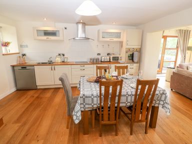 A kitchen with wooden floor a dining table with tablecloth and six chairs at Llofft Yr Yd in Llandwrog near Dinas Dinlle
