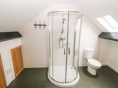 A bathroom with a curved glass shower enclosure and a toilet under a skylight at Llofft Yr Yd in Llandwrog near Dinas Dinlle