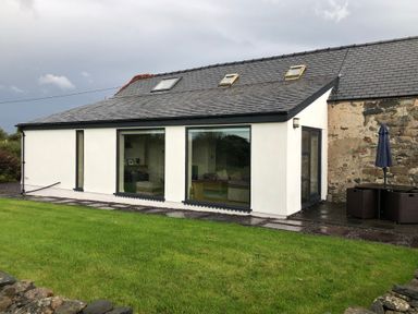 A modern white house with large windows and a stone wall section in a garden at Llofft Yr Yd in Llandwrog near Dinas Dinlle