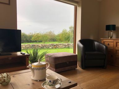 A living room with a teapot and cup on a wooden table overlooking a garden at Llofft Yr Yd in Llandwrog near Dinas Dinlle