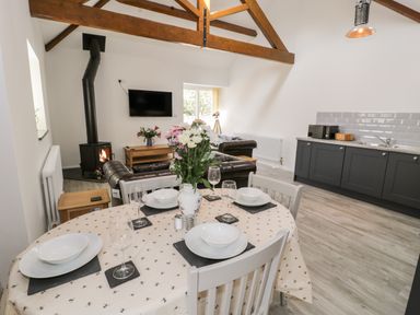 A dining table set with plates bowls and glasses in a living area with sofas a wood stove and kitchen cabinets at 1 Mountain View in Talwrn near Llangefni