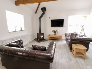 A living room with leather sofas a wood burning stove a mounted television and a telescope at 1 Mountain View in Talwrn near Llangefni