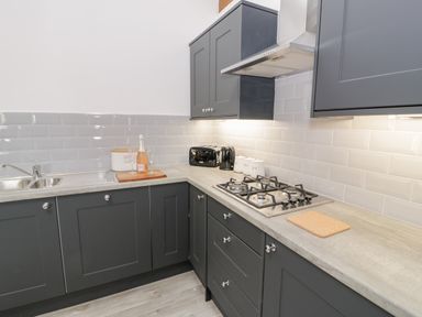 A kitchen corner with dark gray cabinets a gas stove a stainless steel sink a toaster a kettle and jars on the counter at 1 Mountain View in Talwrn near Llangefni