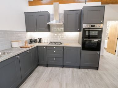 A kitchen with grey cabinets a stove oven toaster kettle and containers at 1 Mountain View in Talwrn near Llangefni