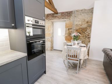 A kitchen area with a dining table set for four and a built-in oven surrounded by grey cabinets at 1 Mountain View in Talwrn near Llangefni