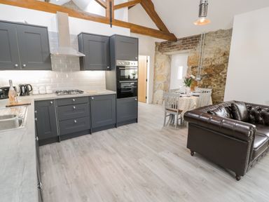 A kitchen with dark cabinets next to a dining table and brown leather sofa at 1 Mountain View in Talwrn near Llangefni