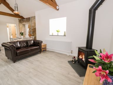 A living room with a brown leather sofa wood burning stove and flowers on a table at 1 Mountain View in Talwrn near Llangefni