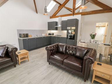 An open plan kitchen and living area with dark grey cabinets brown leather sofas wooden side tables and a dining table with flowers at 1 Mountain View in Talwrn near Llangefni