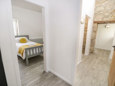 A hallway with stone wall details leading to a bedroom with a gray bed and yellow bedding at 1 Mountain View in Talwrn near Llangefni